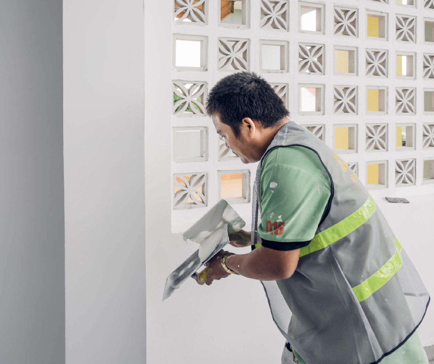 Nhà xây dựng sơn tường gần ô gạch thông gió, mặc áo phản quang, đang làm việc trong công trình xây dựng.