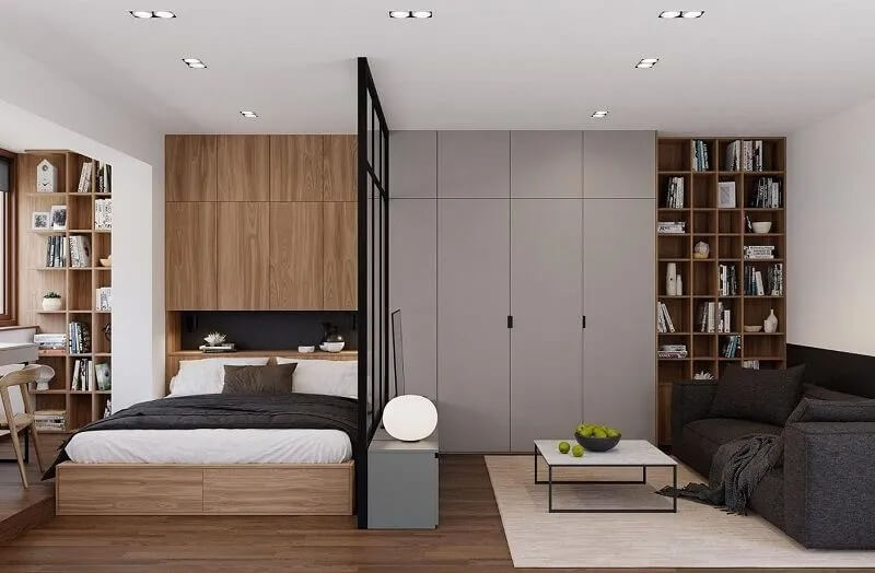 Phòng ngủ hiện đại với giường gỗ, sofa xám, bàn cà phê và giá sách lớn trong không gian mở.