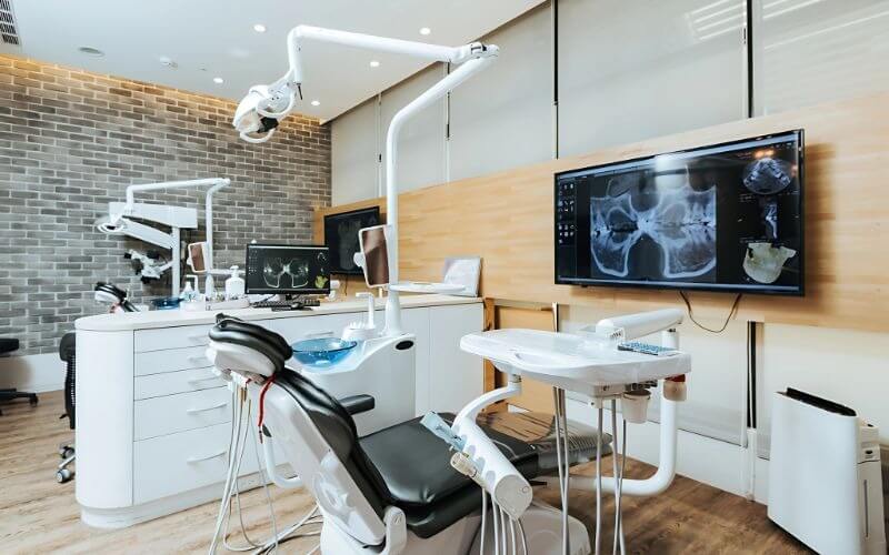 Phòng khám nha khoa hiện đại với ghế khám và màn hình hiển thị X-quang răng, nội thất sáng và sạch sẽ.