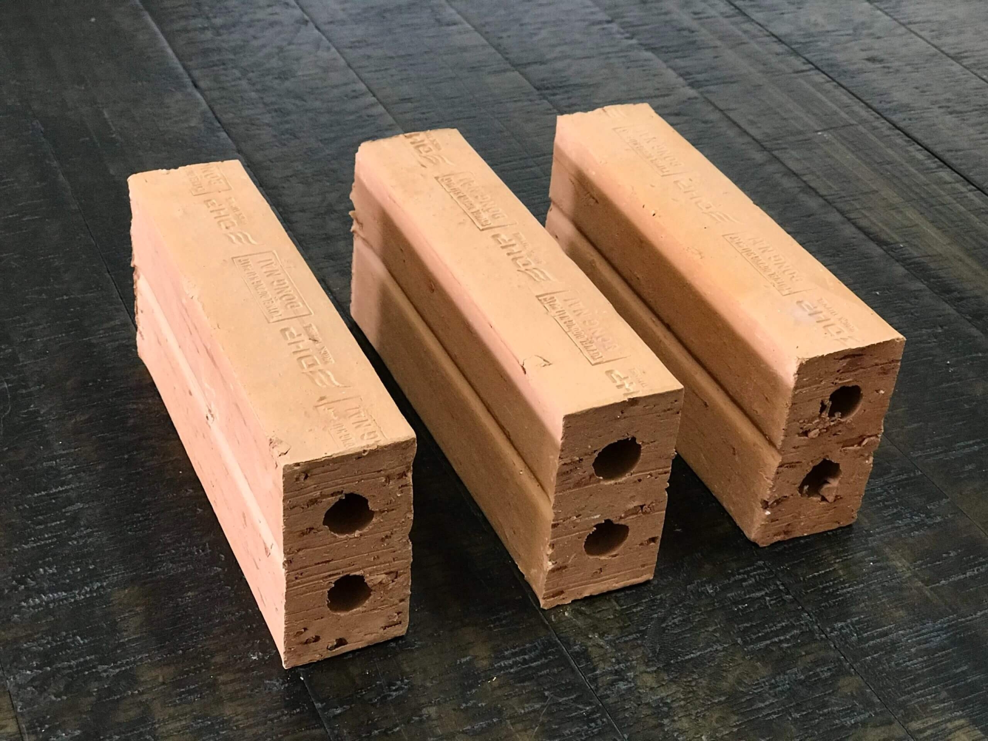 Ba viên gạch đỏ nung có lỗ, xếp thẳng đứng trên nền gỗ tối màu.
