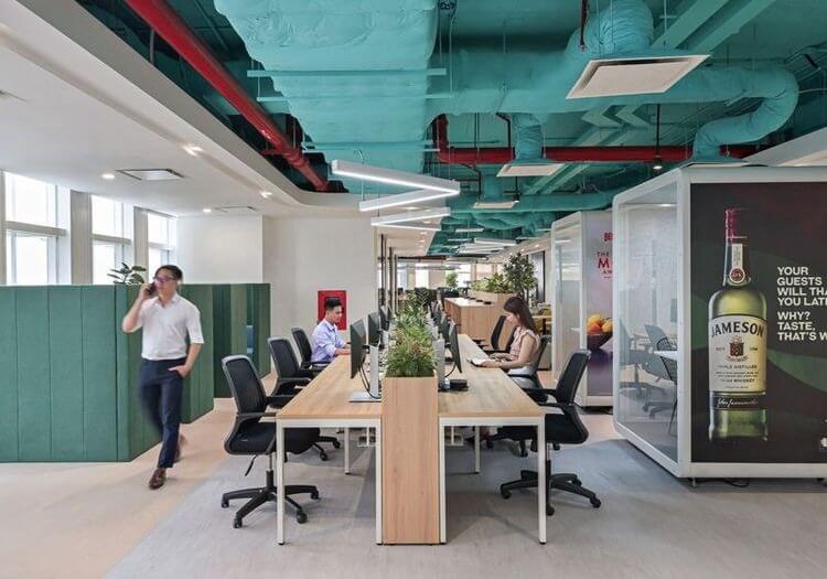 Văn phòng hiện đại với trần xanh, bàn làm việc dài, nhân viên làm việc trên máy tính.