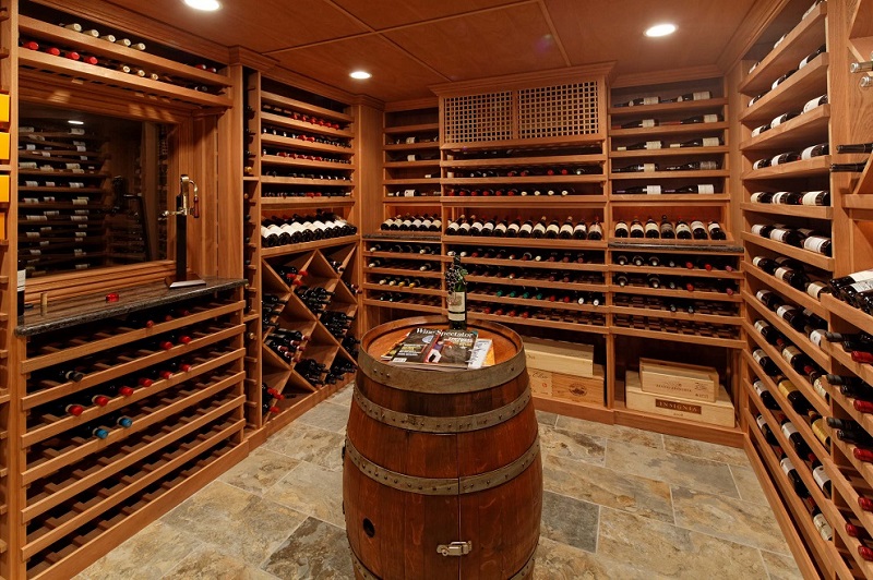 Hầm rượu vang sang trọng với chai rượu trên kệ gỗ và thùng gỗ tròn trung tâm, ánh sáng dịu nhẹ.