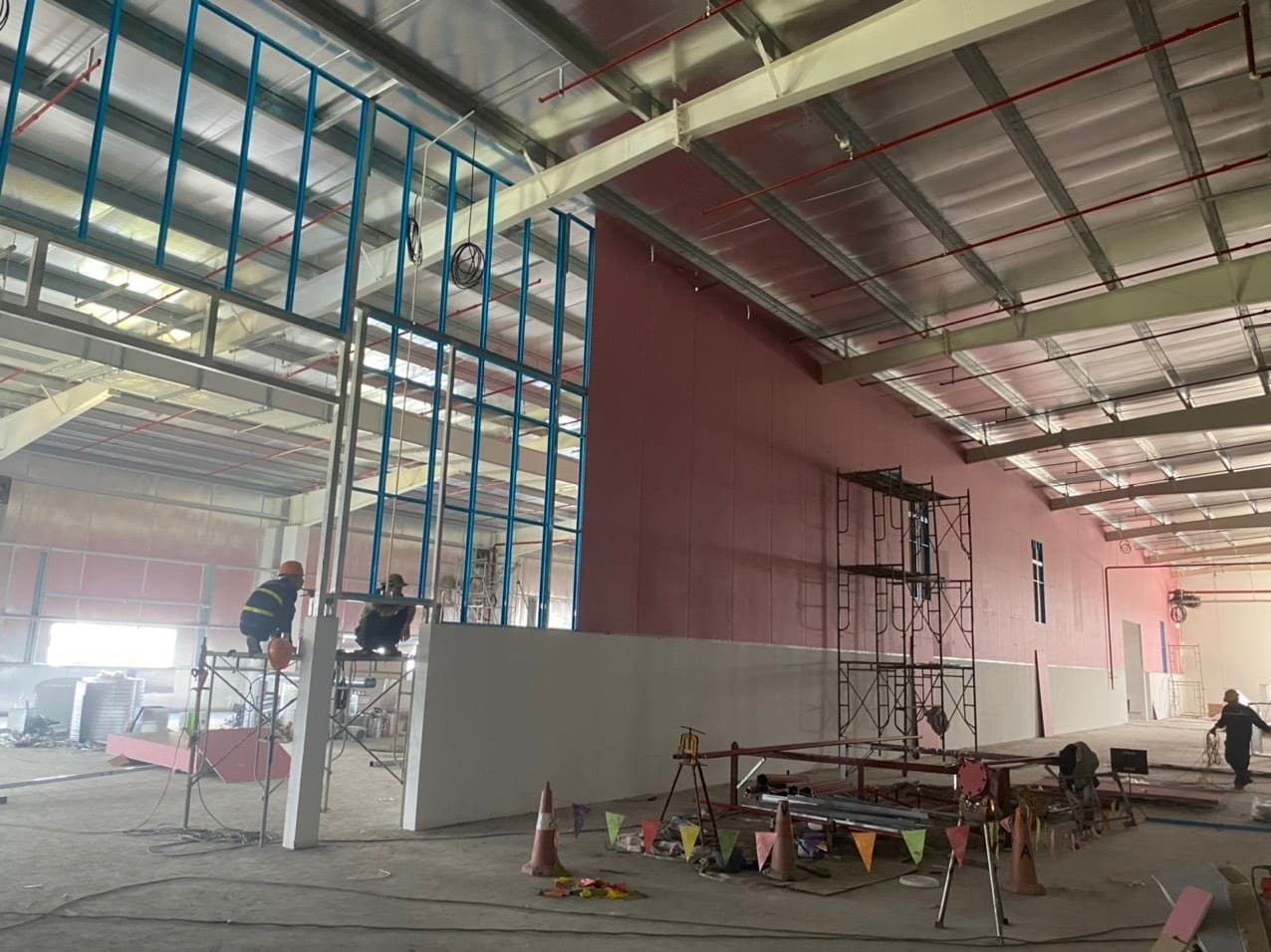 Công nhân đang thi công tòa nhà công nghiệp với cấu trúc thép và tường đang xây dựng.