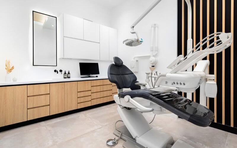 Phòng khám nha khoa hiện đại với ghế nha khoa màu đen và nội thất gỗ sáng, thiết kế tối giản và sạch sẽ.
