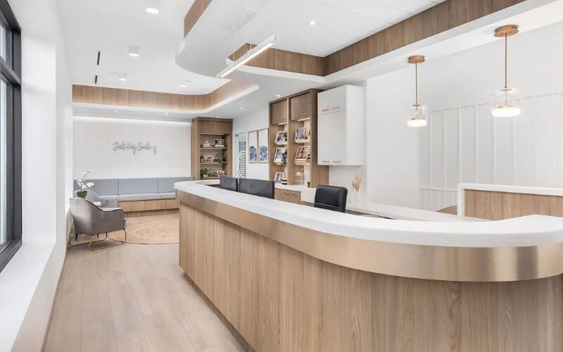Quầy lễ tân hiện đại với nội thất gỗ sáng màu, đèn treo trang trí, không gian rộng rãi và bố trí ngăn nắp.
