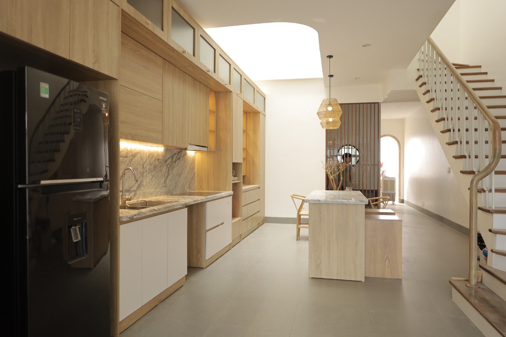phong-bep-dep-nha-ong-16 Nhà bếp hiện đại với tủ gỗ, mặt bàn đá cẩm thạch, đèn trang trí và cầu thang gỗ, tạo không gian thoáng đãng.