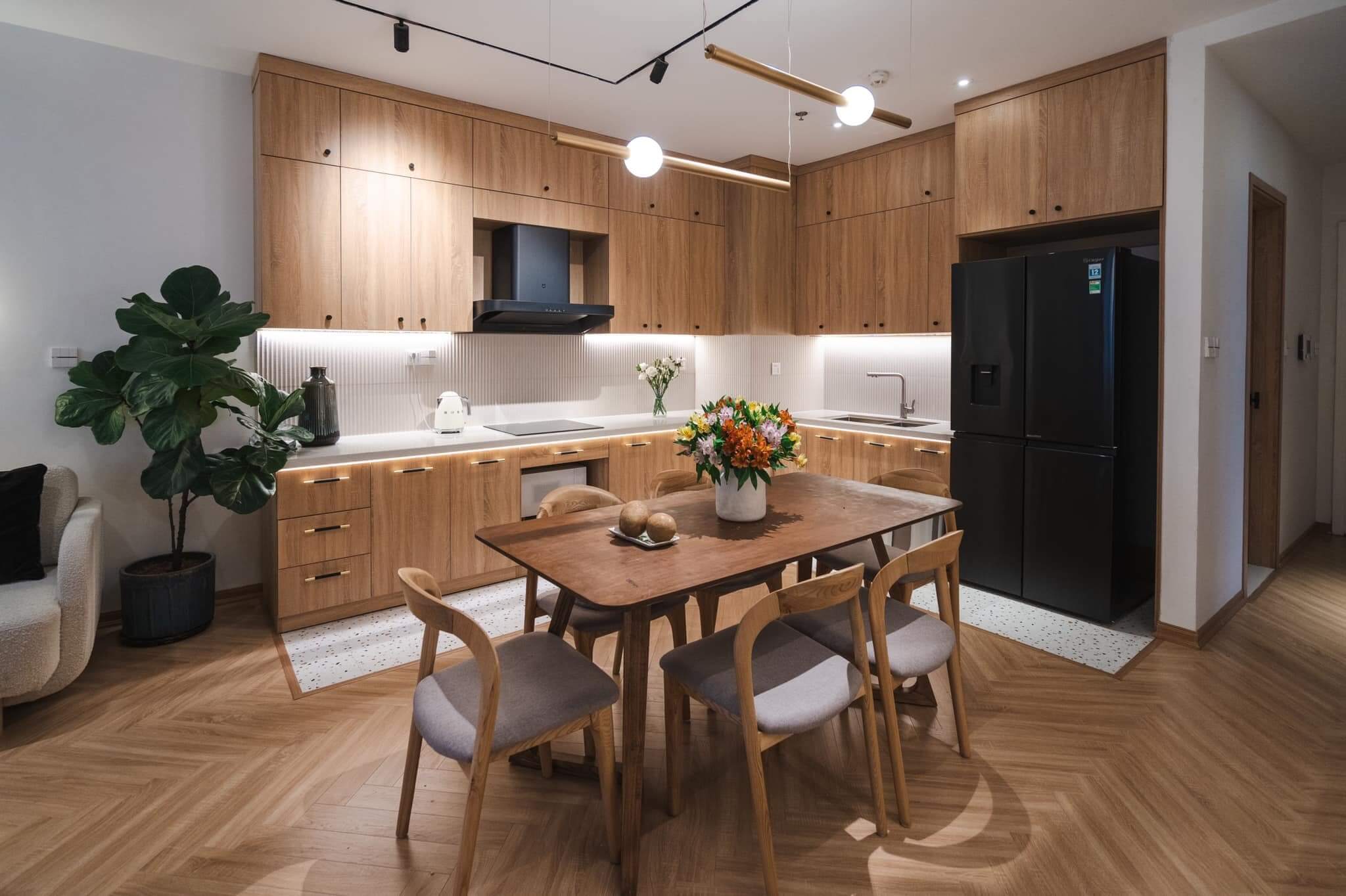 Nhà bếp hiện đại với nội thất gỗ, bàn ăn trang trí hoa tươi, ánh sáng ấm áp.