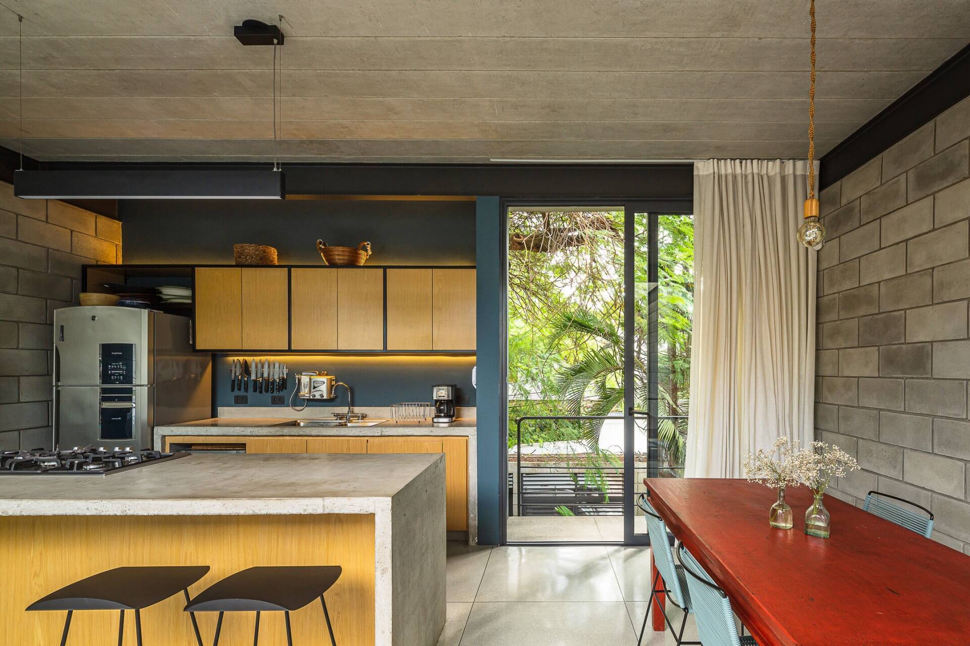 phong-bep-nha-ong-4m-17 Nhà bếp hiện đại với bàn gỗ đỏ và cửa kính lớn nhìn ra khu vườn xanh tươi.