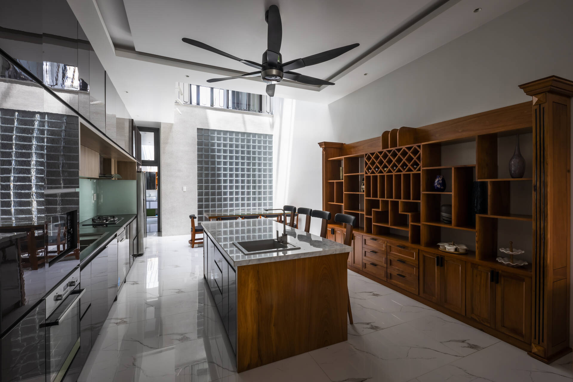Gian bếp hiện đại với tủ gỗ và mặt bàn đá, quạt trần lớn, ánh sáng tự nhiên nổi bật, thiết kế thanh lịch.