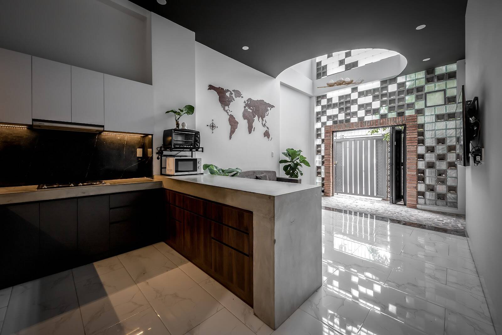 phong-bep-nha-ong-4m-9 Nhà bếp hiện đại với bức tường bản đồ thế giới, cửa chính rộng, nền gạch sáng bóng và cây xanh trang trí.