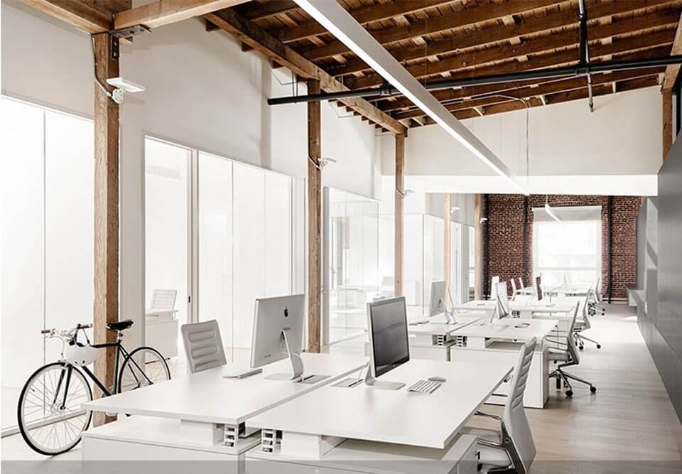 Văn phòng hiện đại với bàn trắng, máy tính, ghế xoay và xe đạp trong không gian mở và thoáng đãng.