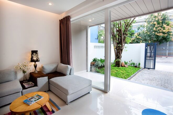 Phòng khách hiện đại với sofa xám, cửa kính lớn nhìn ra vườn xanh mát.