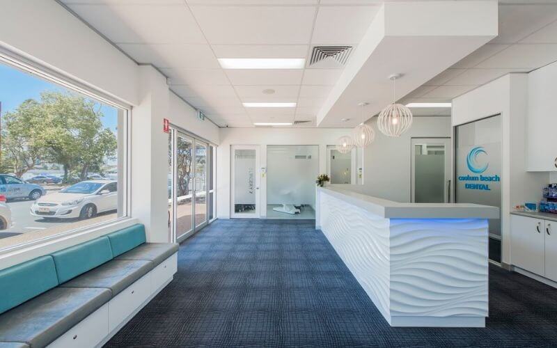 Phòng chờ hiện đại với quầy lễ tân và ghế dài xanh, ánh sáng tự nhiên từ cửa sổ lớn nhìn ra bên ngoài.