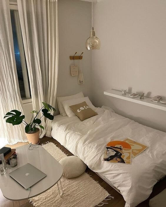 phong-ngu-15m2-co-nho-khong Phòng ngủ tối giản với giường trắng, bàn laptop và cây xanh, tạo cảm giác thoải mái và thư giãn.