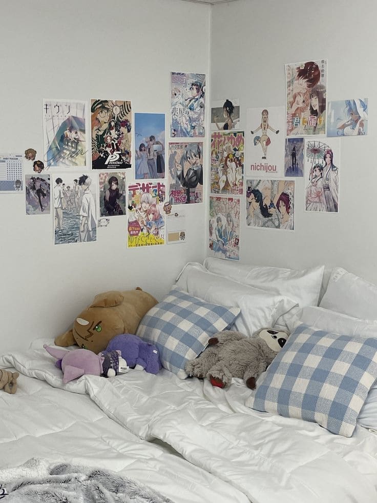 Giường ngủ với gối kẻ caro xanh, thú nhồi bông, tường trang trí bằng poster anime nhiều màu sắc.