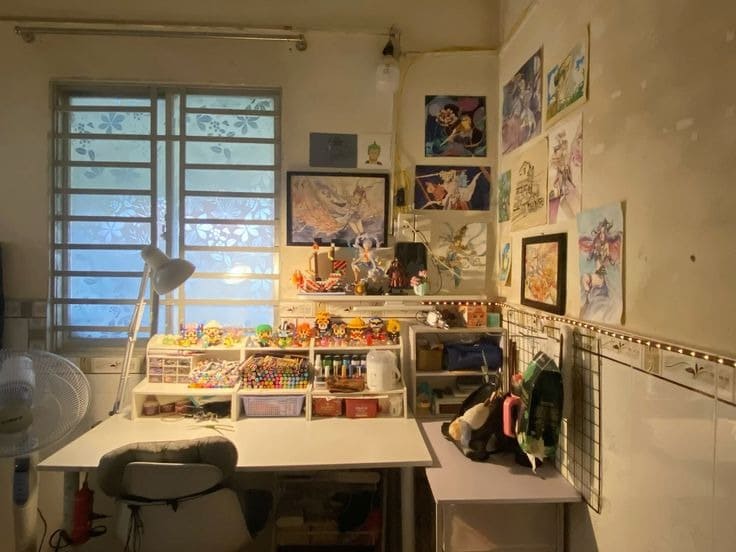 Góc làm việc sáng tạo với bàn trắng, tranh treo tường và dụng cụ nghệ thuật dưới ánh sáng cửa sổ.