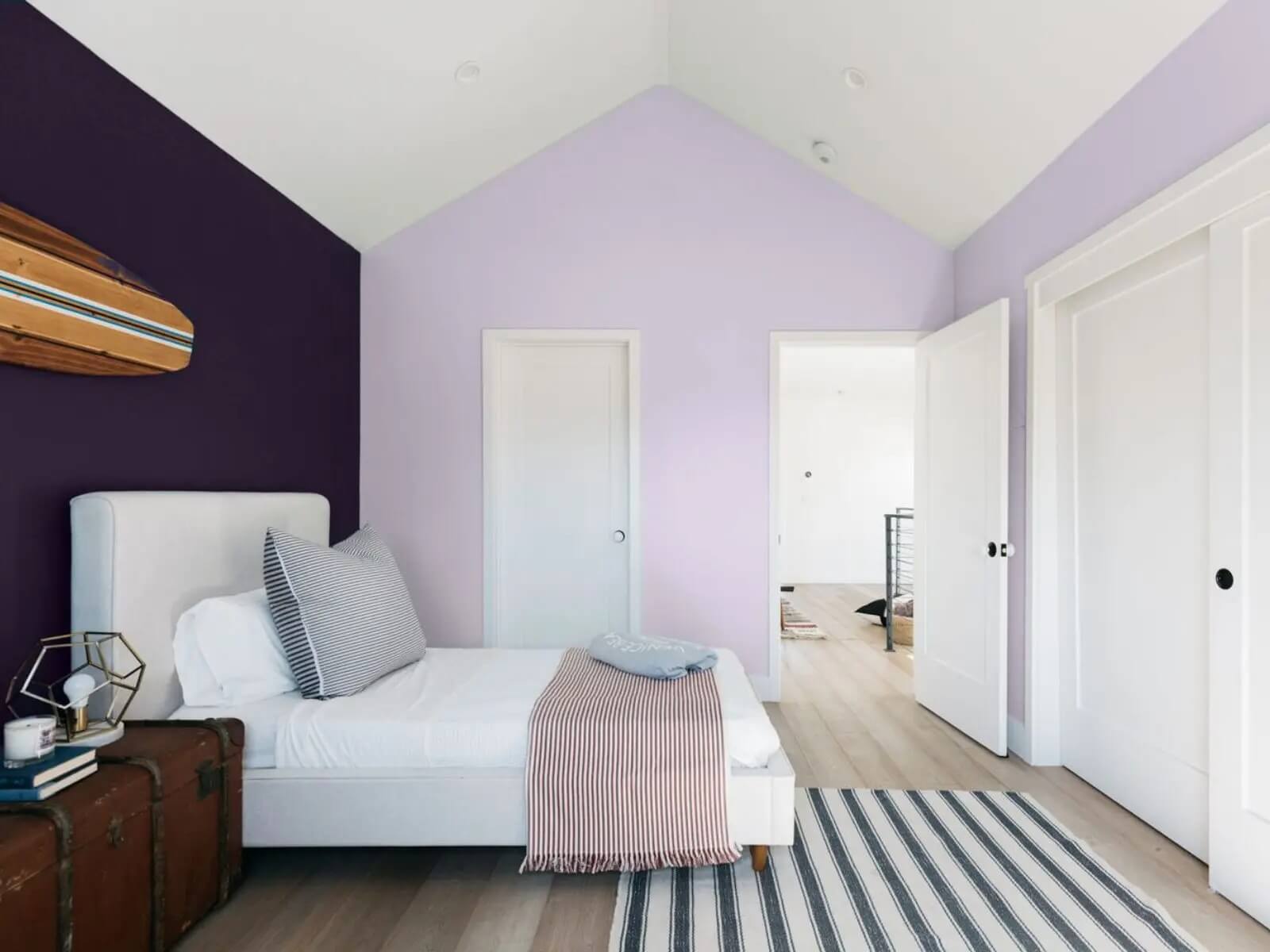 Phòng ngủ hiện đại với tường tím, giường trắng, thảm kẻ sọc và đồ trang trí hiện đại.