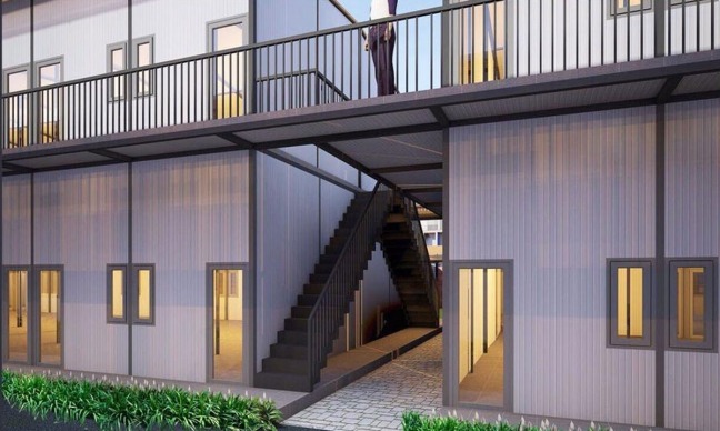 phong-tro-2-tang Tòa nhà lắp ghép hiện đại với cầu thang giữa, bao quanh bởi hành lang và cửa sổ, cây xanh phía trước.