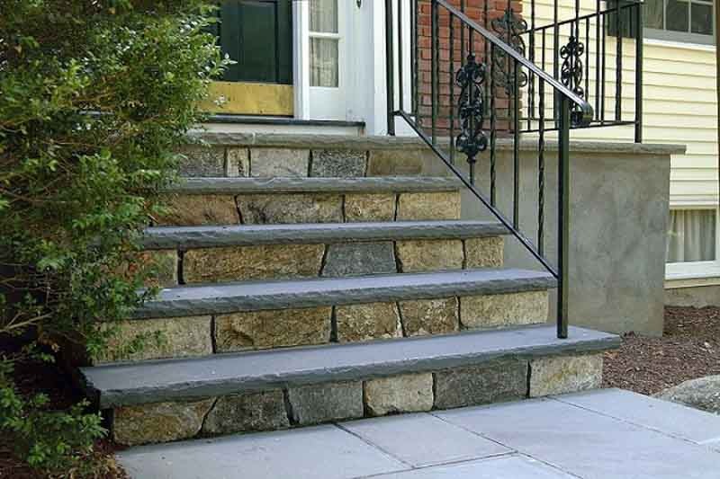 Cầu thang đá ngoài trời với lan can sắt đen tại lối vào một ngôi nhà.