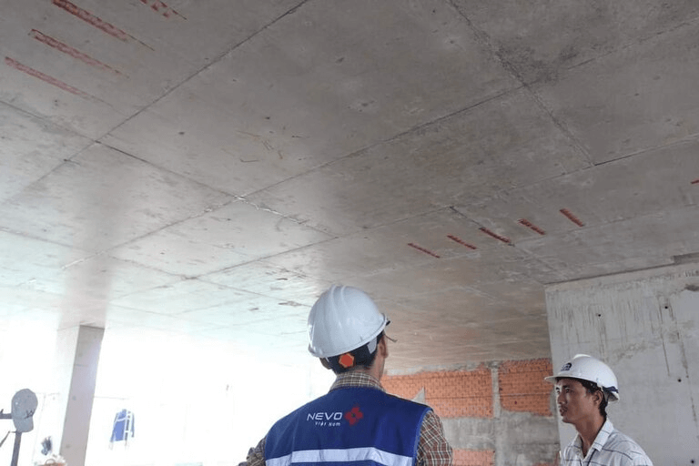 Hai công nhân xây dựng đội mũ bảo hộ kiểm tra trần bê tông tại công trường.