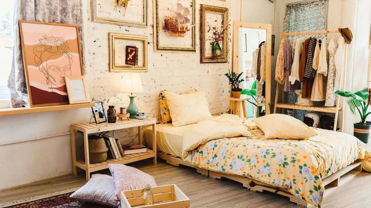 Phòng ngủ phong cách boho với giường hoa, tranh nghệ thuật, quần áo treo, cây xanh và đèn bàn.