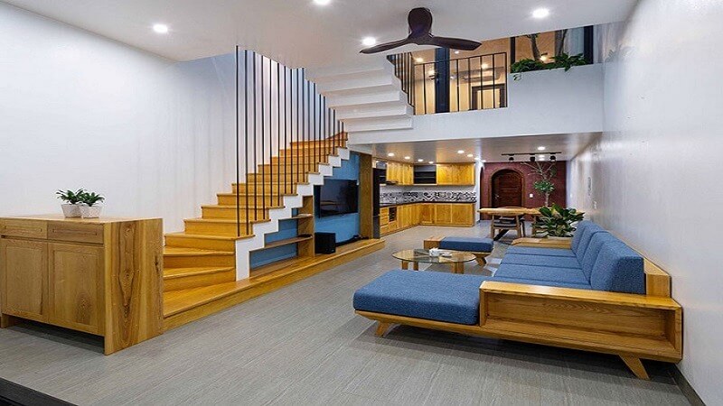 Phòng khách hiện đại với cầu thang gỗ, sofa xanh và nội thất tối giản, không gian thoáng đãng và sáng sủa.