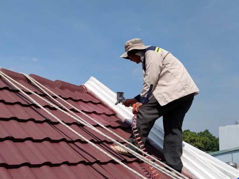 rui-ro-va-hau-qua-khi-nang-mai-nha-khong-xin-phep Người thợ đang sơn mái tôn màu đỏ dưới trời xanh, đội mũ bảo hộ và mặc áo khoác dài.