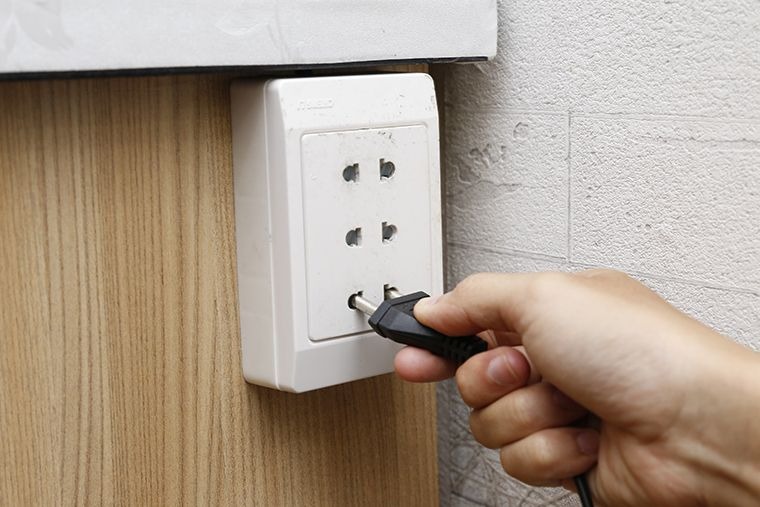 Cắm phích điện vào ổ cắm trên tường bằng tay người, cảnh minh họa sử dụng thiết bị điện an toàn.