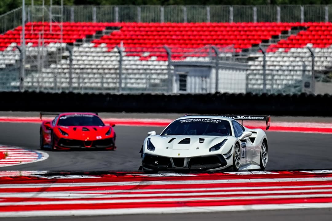 Hai xe đua tốc độ cao trên đường đua với khán đài vắng phía sau.