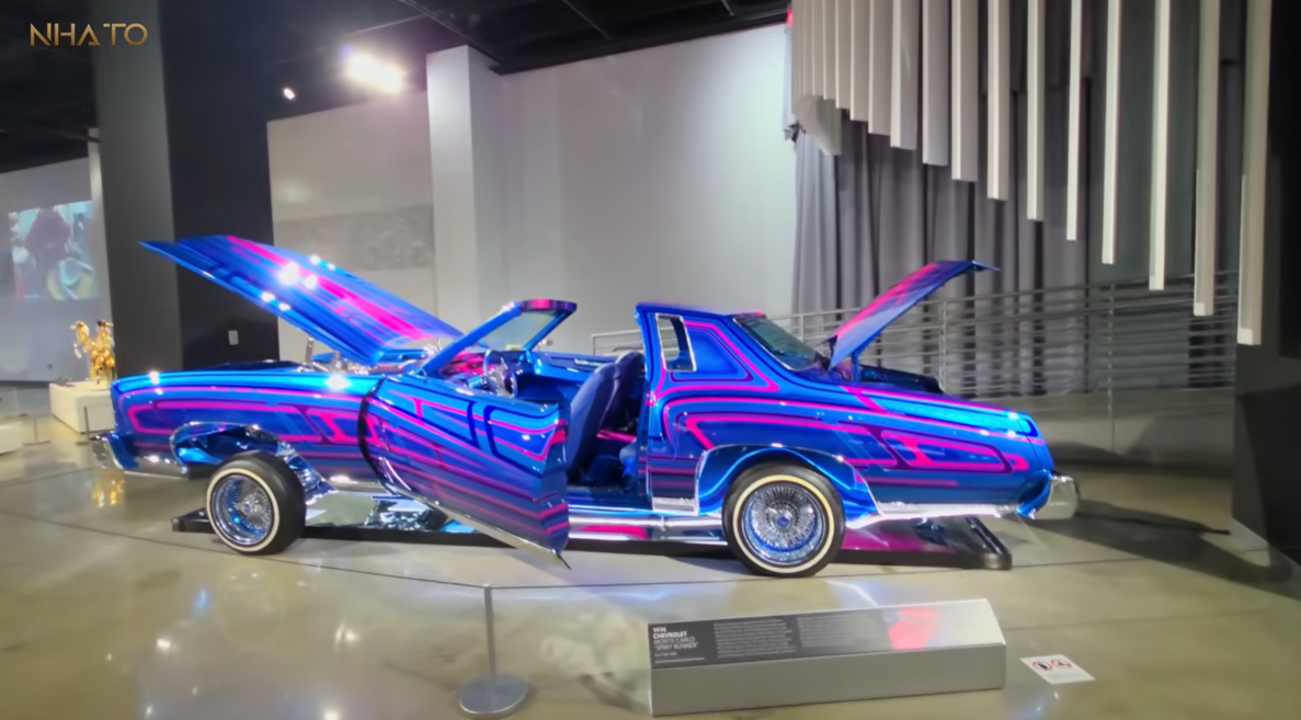 screenshot-2025-07-08-154007 Xe Chevrolet cổ điển độ màu xanh tím, cửa mở tung, trưng bày tại triển lãm nghệ thuật ô tô.