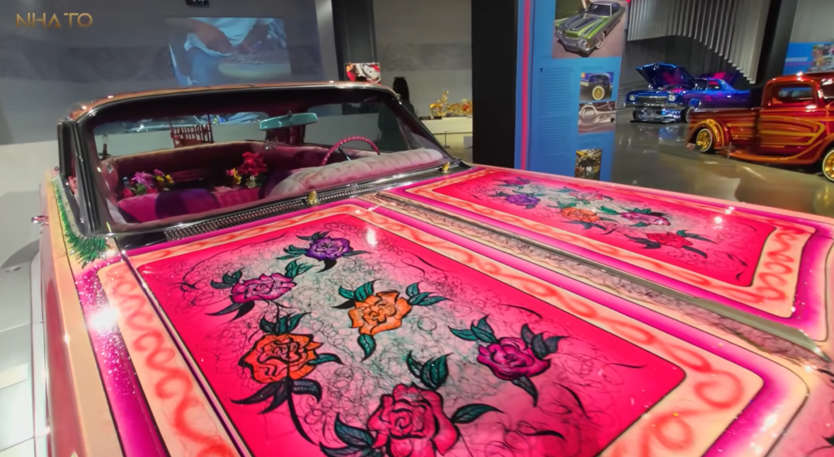 screenshot-2025-07-08-154126 Xe hơi cổ điển với nắp capo màu hồng và hoa văn hoa rực rỡ trong bảo tàng ô tô.