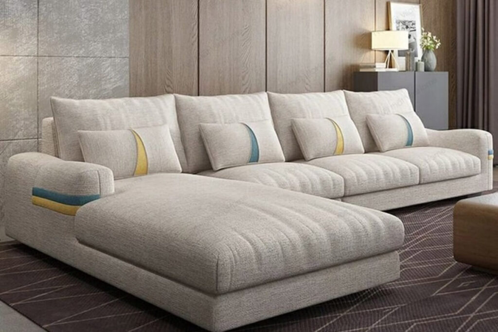 Sofa góc lớn màu be với gối tựa trang trí trong phòng khách hiện đại, sàn thảm tối màu.