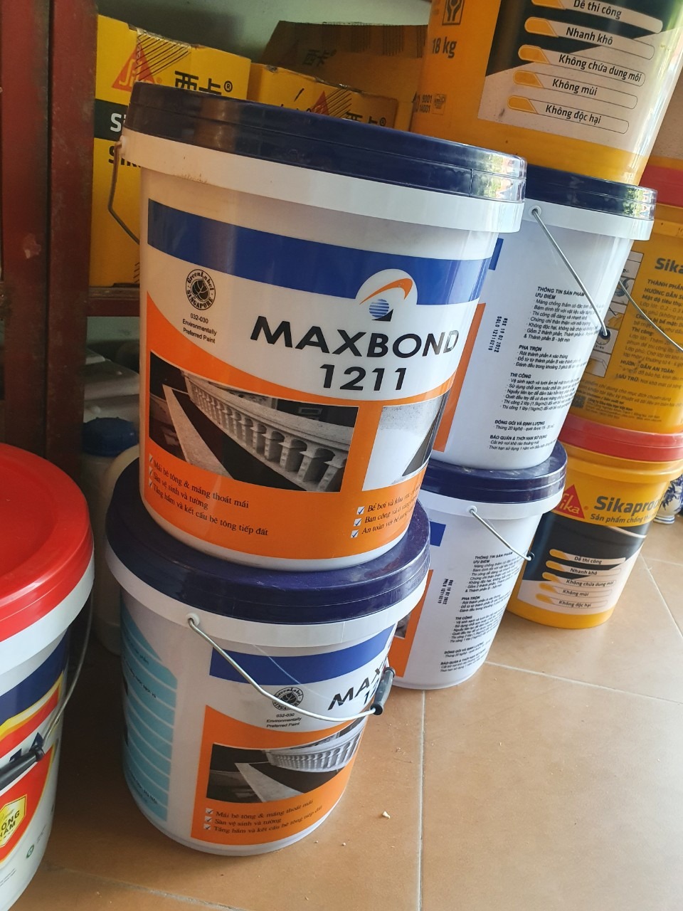 Các thùng sơn Maxbond 1211 và Sikaproof trên sàn gạch, dùng trong xây dựng và chống thấm.