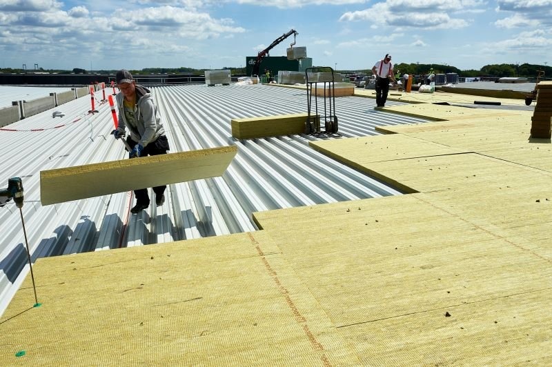 Công nhân đang lắp đặt tấm cách nhiệt trên mái nhà công nghiệp dưới trời nắng.
