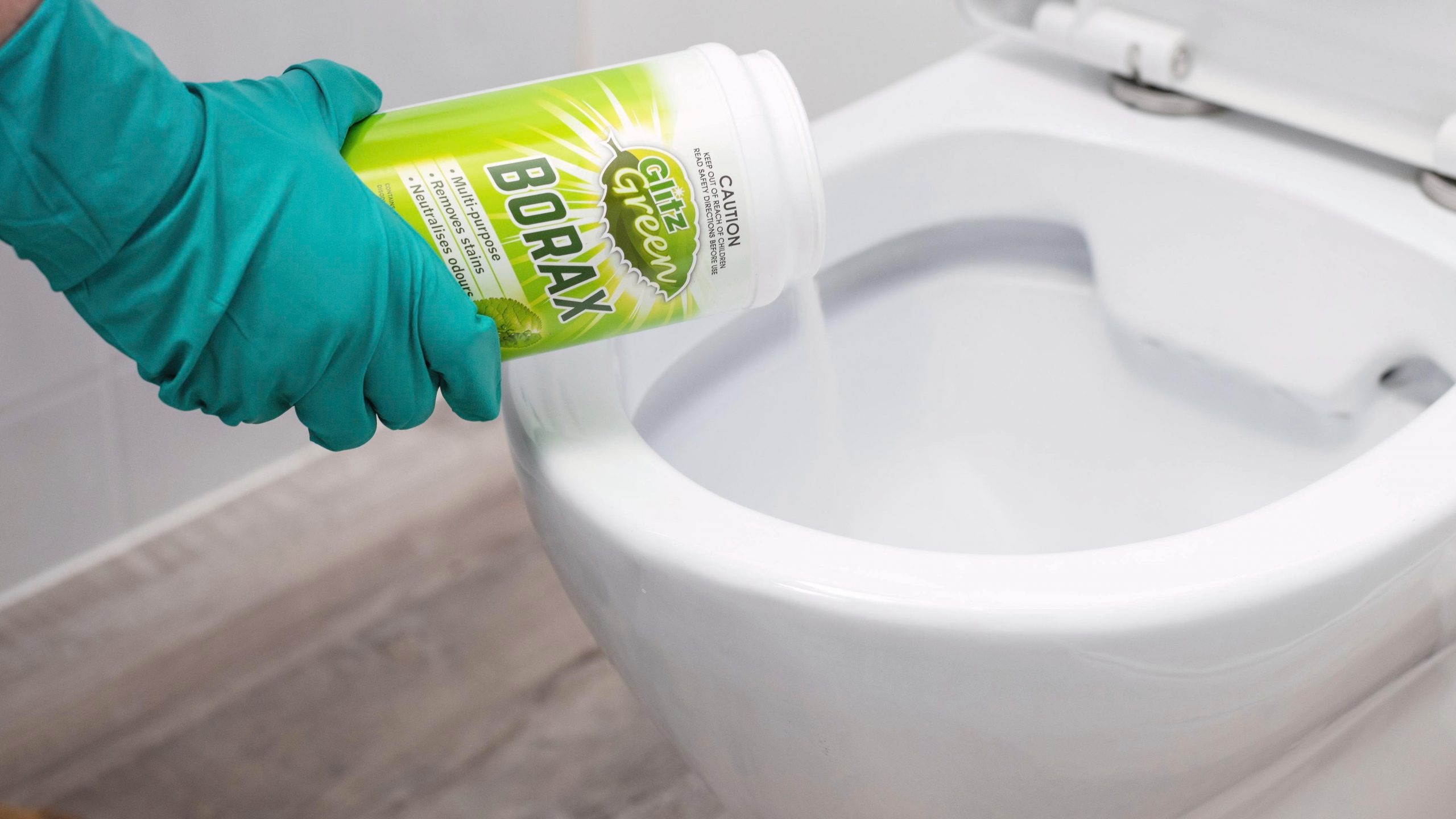 su-dung-bot-giat-tay-trang-nap-nhua-bon-cau Người đeo găng tay xanh đổ bột borax vào bồn cầu trắng để làm sạch và khử trùng.