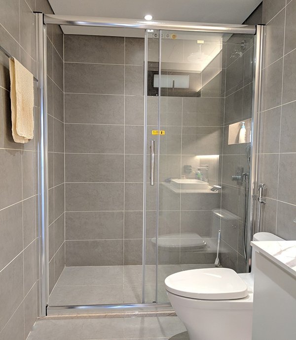 Phòng tắm hiện đại với buồng tắm kính, tường lát gạch xám và bồn cầu trắng.