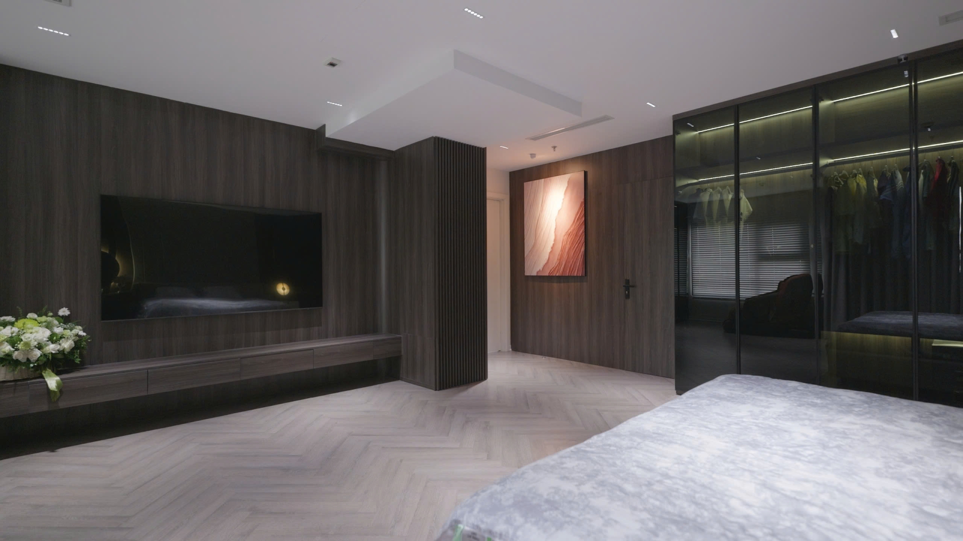 sz7fkc3jrv1olemubphd Phòng ngủ hiện đại với tường gỗ, tivi lớn, tranh nghệ thuật và tủ quần áo kính.