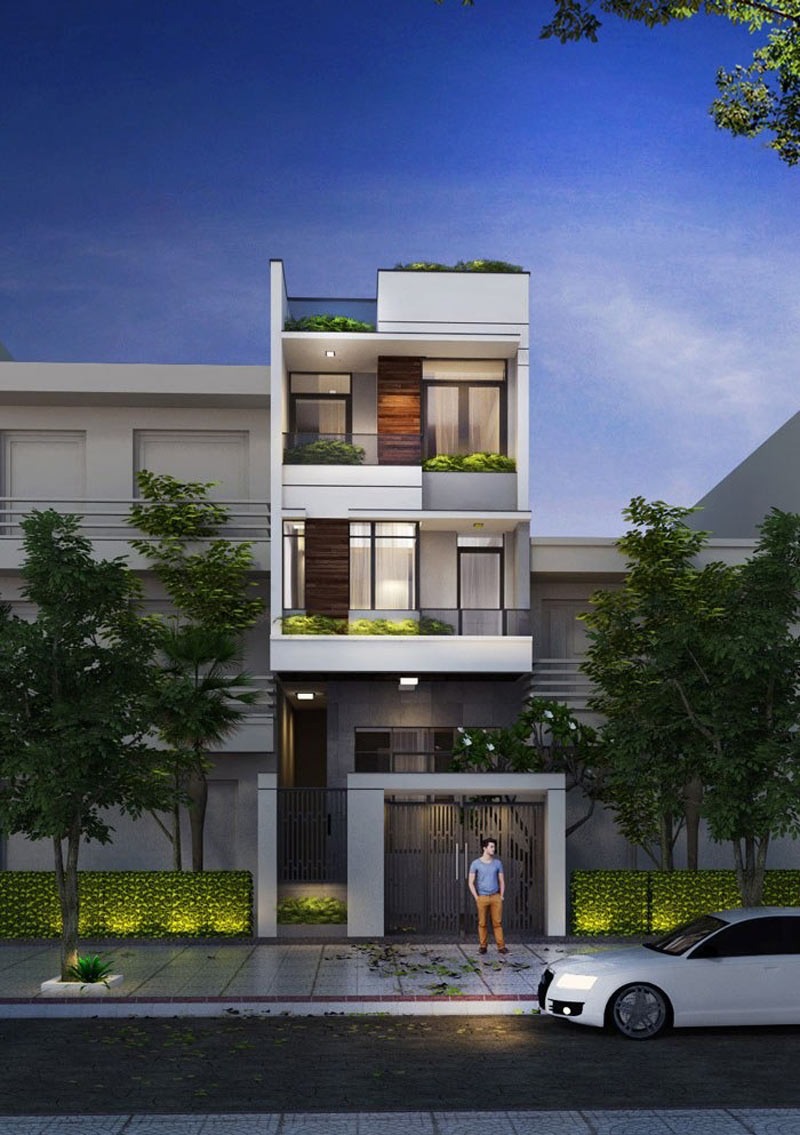 Nhà phố hiện đại ba tầng với cây xanh, buổi tối, người đứng trước cổng, ô tô trắng đậu ngoài đường.