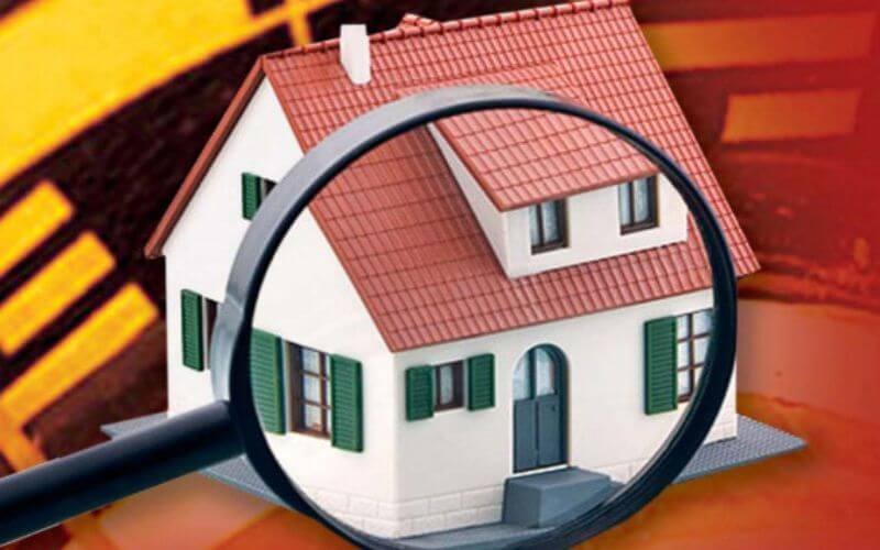 Kính lúp phóng đại ngôi nhà mô hình mái ngói đỏ, cửa chớp xanh, trên nền màu cam.