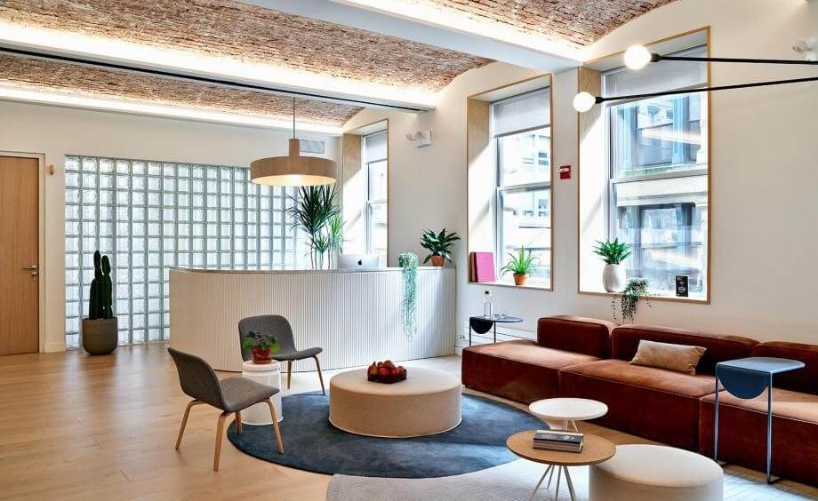 Phòng khách hiện đại với sofa nâu, bàn tròn và cây cảnh, ánh sáng tự nhiên từ cửa sổ lớn.