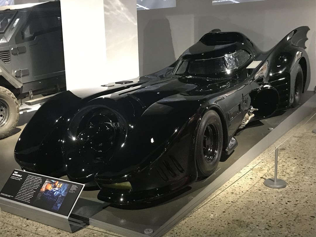 the-89-batmobile-at-the-petersen Xe Batmobile màu đen bóng trong bảo tàng, nổi bật với thiết kế tương lai và ánh sáng phản chiếu.