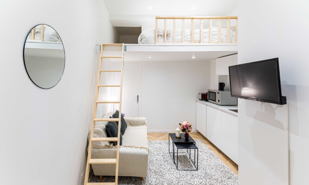 Căn hộ nhỏ có gác xép với ghế sofa, cầu thang gỗ, và bếp nhỏ, không gian hiện đại, tiện nghi.