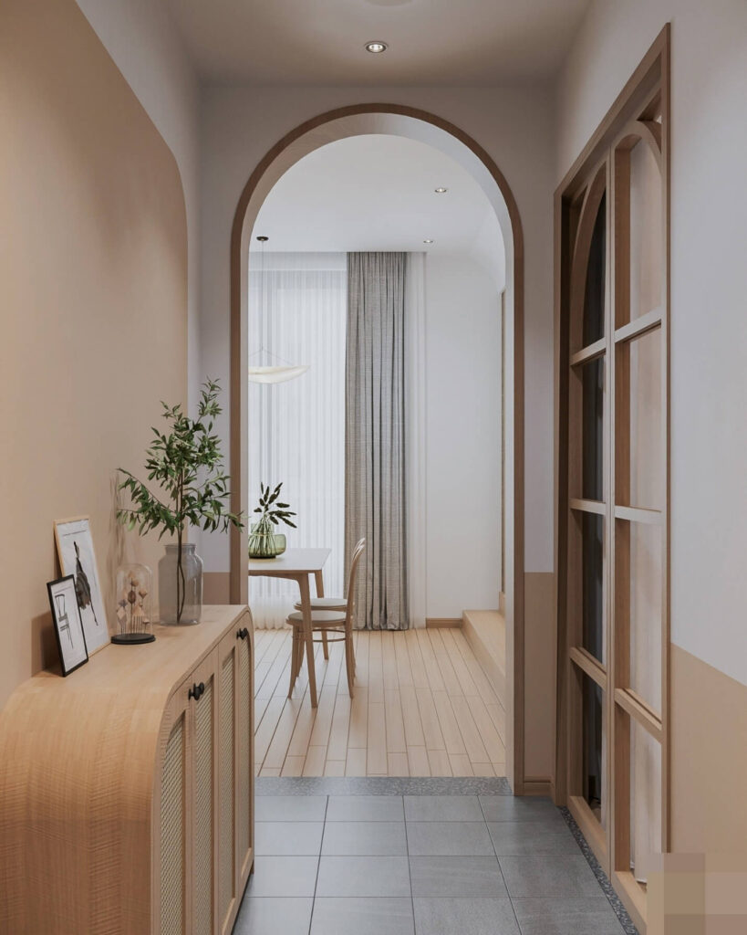 Hành lang tối giản với tủ gỗ, cây xanh, và cửa vòm dẫn vào phòng ăn sáng ánh sáng tự nhiên.