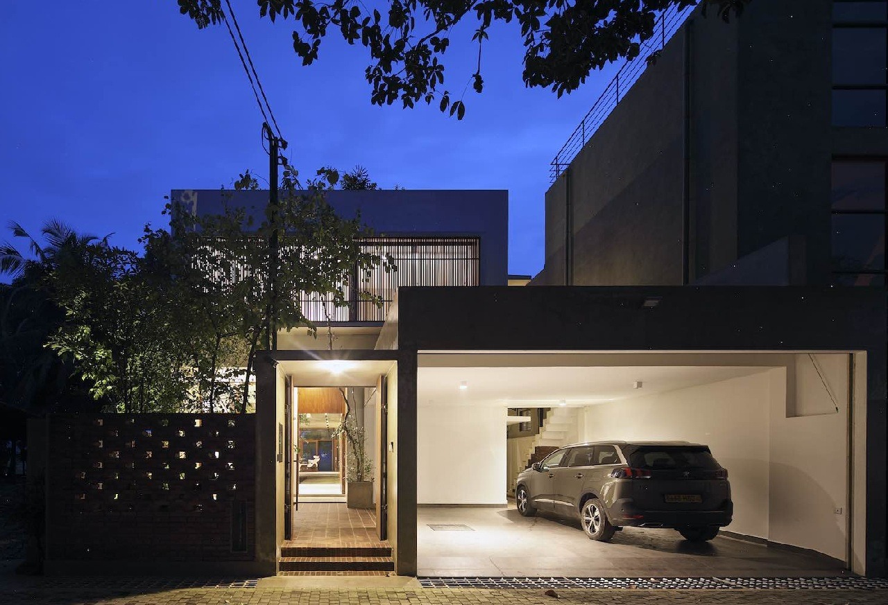 Ngôi nhà hiện đại với gara rộng rãi, ánh sáng ấm áp trong buổi tối, cây xanh bao quanh.