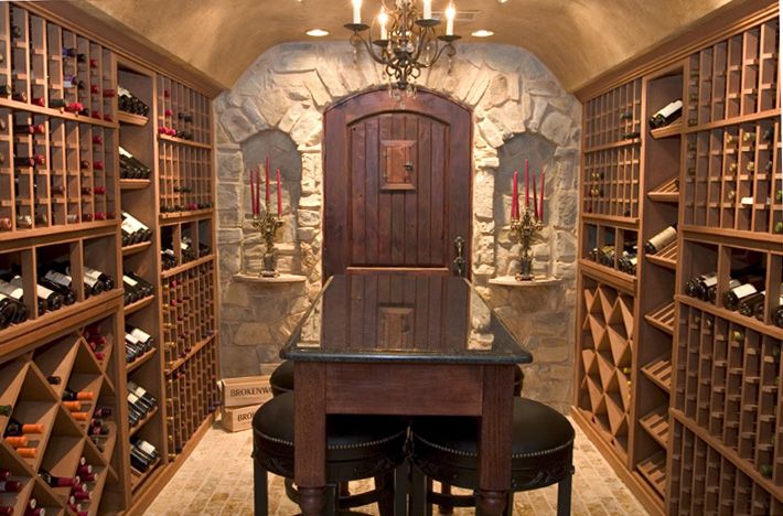 Hầm rượu vang sang trọng với kệ gỗ và ánh sáng êm ái, bàn trung tâm, đèn chùm và nến tạo không khí cố điển.