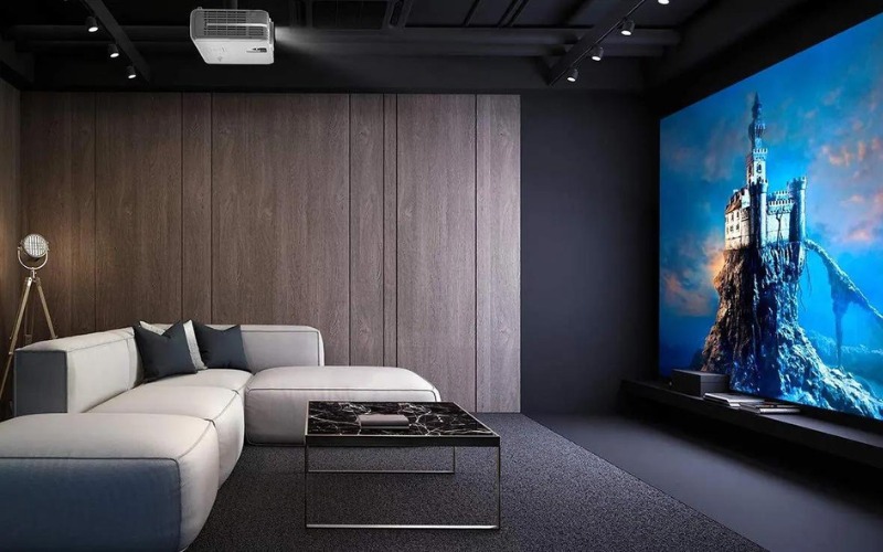 thiet-ke-khong-gian-phong-giai-tri Phòng khách hiện đại với sofa trắng, bàn đá và máy chiếu lớn chiếu cảnh lâu đài trên núi.