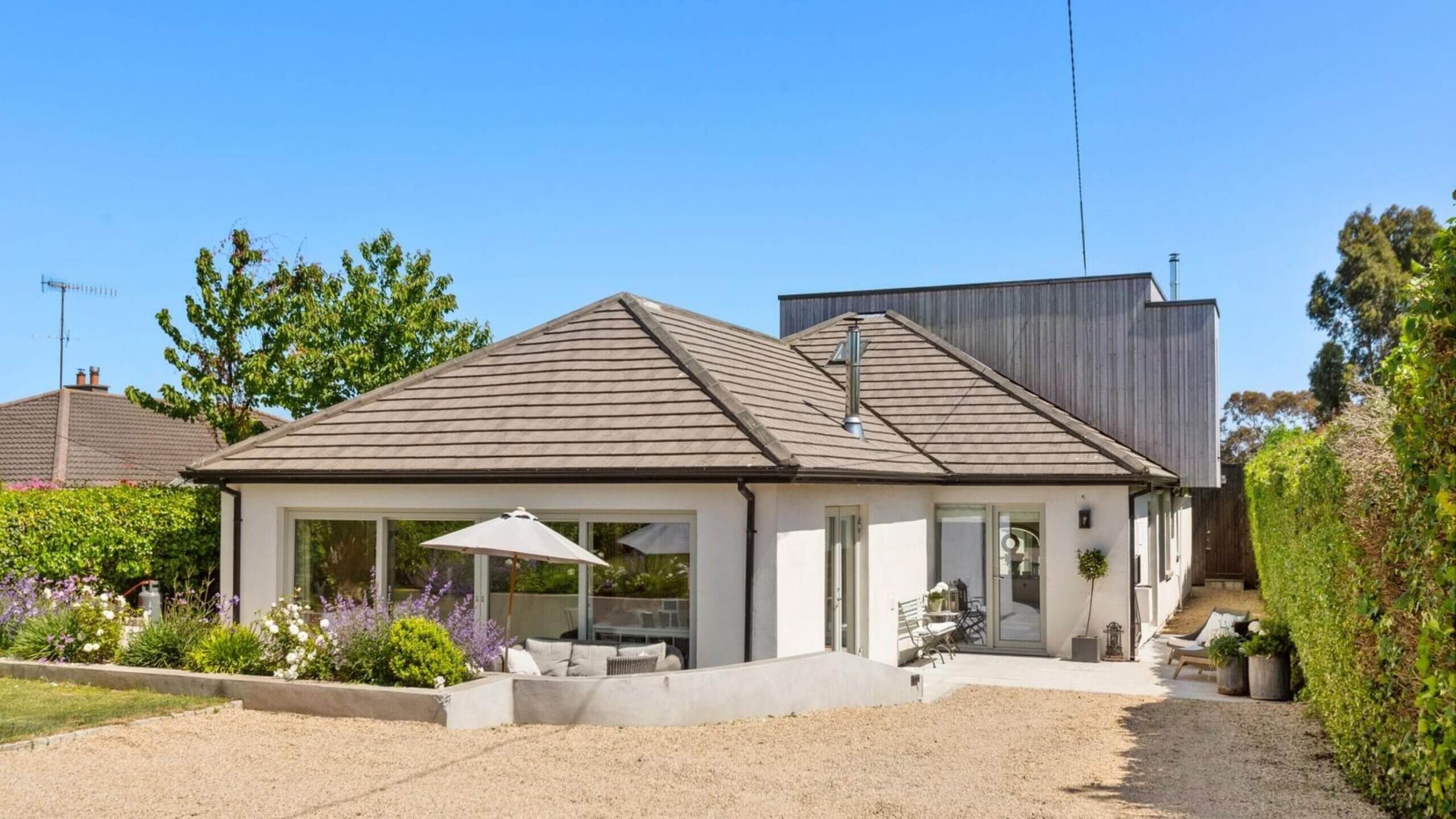 Ngôi nhà mái ngói hiện đại với sân vườn, cây xanh xung quanh và ghế ngồi ngoài trời.