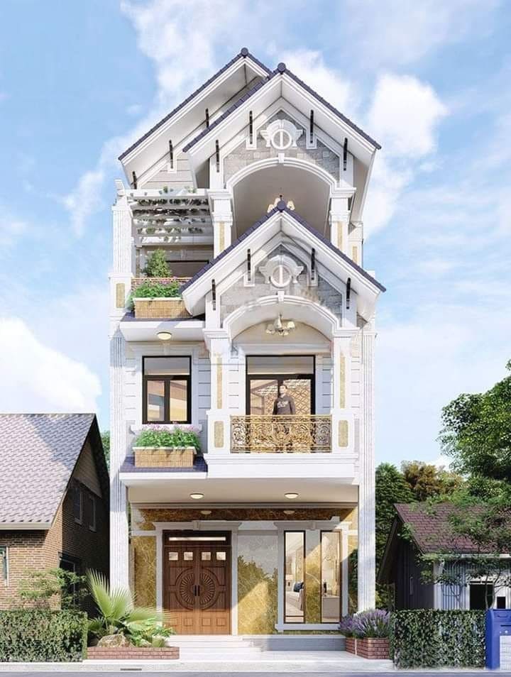 Nhà phố 3 tầng mái thái hiện đại, có ban công, cửa sổ kính và trang trí cây xanh.