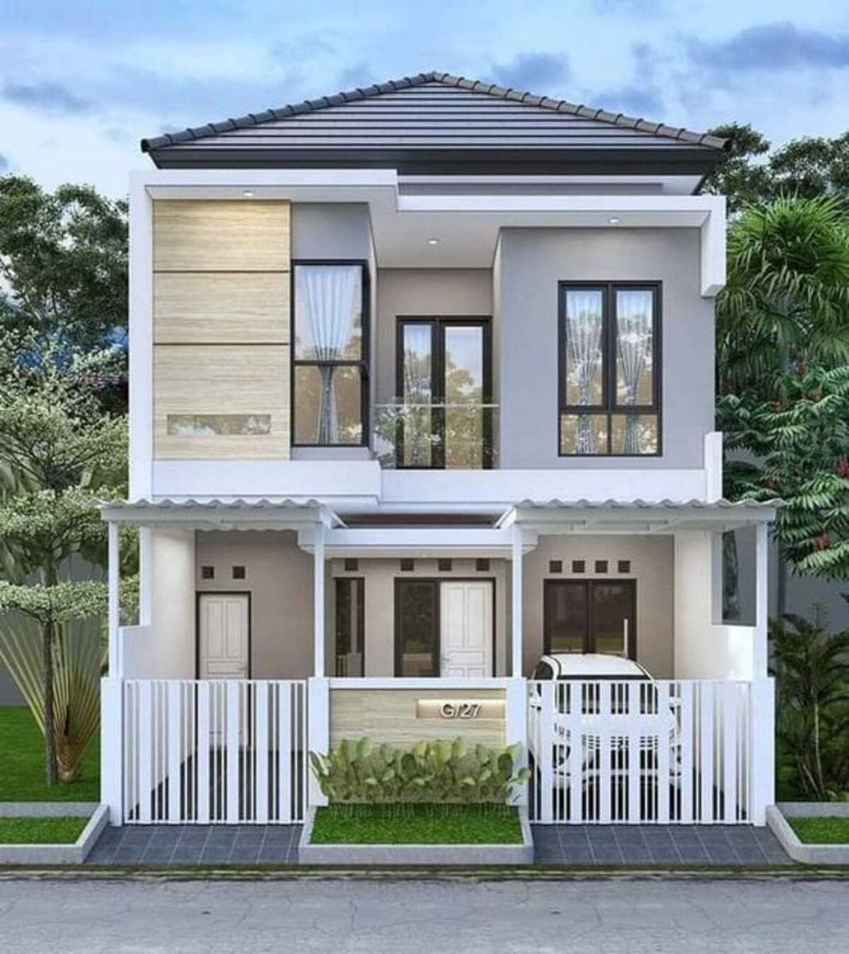 Nhà hai tầng hiện đại với cửa kính và mái ngói, sân trước có hàng rào trắng và cây xanh ở bên cạnh.