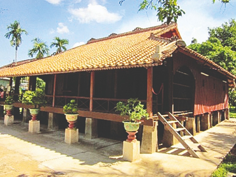 Nhà sàn truyền thống Việt Nam với mái ngói đỏ tươi, xung quanh là cây cảnh và trời xanh nắng đẹp.